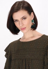 Ciemnozielona bluzka z okrągłym dekoltem, falbanistymi rękawami, wzorem teksturowym oraz dekoracyjnymi koronkowymi akcentami.