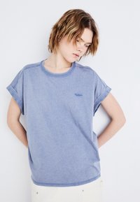 Tricou scurt cu mânecă, de culoare albastru deschis, realizat dintr-un material moale. Are un guler rotund, mâneci răsucite și un detaliu mic cu logo pe piept.