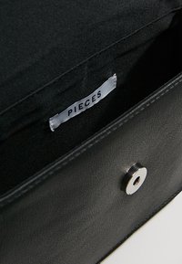 Wnętrze czarnej torby z ekologicznej skóry z materiałową podszewką. Wyposażone w zapięcie na zatrzask oraz białą metkę z napisem „PIECES” wewnątrz.