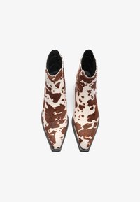 Μπότα από δέρμα αγελάδας μέχρι τον αστράγαλο με μυτερή μύτη, σε καφέ και λευκό μοτίβο με βούλες και μαύρη καουτσούκ σόλα. Λείος υφή.