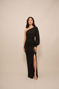 Black one-shoulder dress with a fitted design, featuring a draped long sleeve, a high slit, and a smooth texture. Heeled sandals visible.