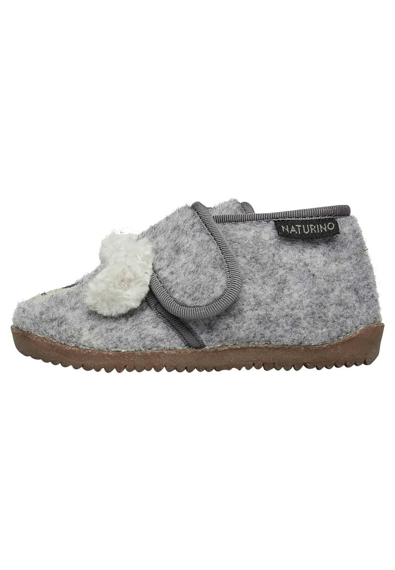 Zapatilla infantil de felpa gris con superficie texturizada, con un pom-pom de felpa, correa ajustable y suela de goma para mayor agarre.
