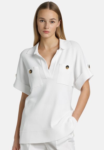 Weiße kurzärmlige Bluse mit kragenförmigem Ausschnitt, zwei Brusttaschen und Akzenten in Goldfarbe, aus einem strukturierten Material.