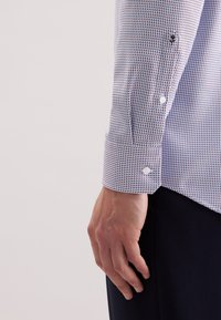 Camicia button-up con un motivo geometrico blu e bianco, dotata di colletto classico, bottoni ai polsini e vestibilità slim. Texture morbida in cotone.