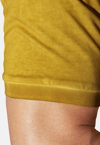 Mustard yellow shorts with a textured fabric, featuring a ribbed waistband and a close-fitting design. Smooth skin visible above.
