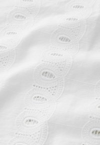Tissu blanc avec des détails brodés présentant un design en dentelle et des découpes œillets, créant texture et motif. Fini en coton lisse.