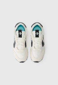 Baskets de sport blanches et noires avec une tige texturée, des accents noirs sur les côtés et une semelle intérieure à motif bleu. Fermeture à lacets.
