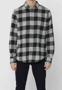 Camisa de pliegue en patrón de cuadros negro y gris, con mangas largas, puños abotonados y dobladillo recto. Fabricada en una suave tela texturizada.