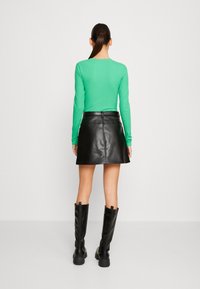 Groene geribbelde lange mouw top, zwarte leren mini rok en zwarte kniehoge laarzen. Eenvoudig ontwerp met een aansluitende silhoutte.