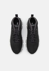 Černé nubukové tenisky s texturovaným povrchem, plochými tkaničkami a bílou gumovou podrážkou. Obsahují logo na jazyku a poutko.