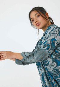 Textured garment featuring a blue and gray swirling pattern, with puffed sleeves and a loose fit. Soft fabric visible throughout.