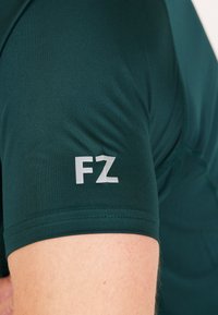 Grön atletisk tröja med korta ärmar, med en texturerad tyg och en vit "FZ"-logotyp på vänster ärm.