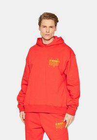 Felpa con cappuccio rossa realizzata in tessuto morbido, con un logo grafico giallo sul petto. Vestibilità ampia con polsini e orlo a coste.