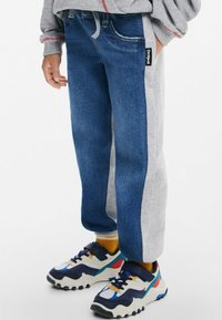 Šedá bavlněná mikina s jogger kalhotami ve stylu džínsů v modro-šedé barevné kombinaci. Černý štítek na boku. Barevné tenisky s akcenty.