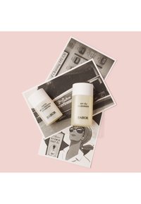 Dos productos de cuidado de la piel de Babor: una pequeña botella blanca etiquetada como "PHYTO HYDRO BOOSTER" y una botella translúcida más grande etiquetada como "HY-ÖL CLEANSER". Ambos reposan sobre postales vintage en blanco y negro sobre una superficie rosa.