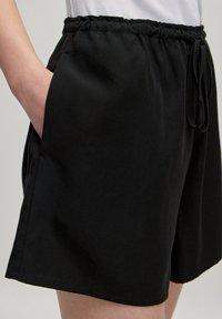 Zwarte shorts van lichtgewicht stof, met een elastische tailleband met trekkoord, zijzakken en een relaxed fit.