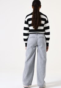 Gestreifter Pullover in Schwarz-Weiß, kombiniert mit hellgrauen, weit geschnittenen Jeans. Die Jeans haben Gesäßtaschen und einen lockeren Schnitt. Einfaches, lässiges Design.