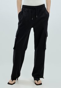 Zwarte lichtgewicht cargo-broek met een elastische tailleband, zijzakken en ritsaccenten bij de enkels. Heeft een ontspannen pasvorm.