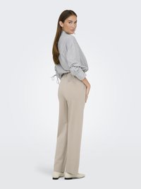 Blouse à rayures à manches longues avec des accents à cordon, associée à un pantalon large beige, portée avec des chaussures claires, mettant en valeur une coupe décontractée.