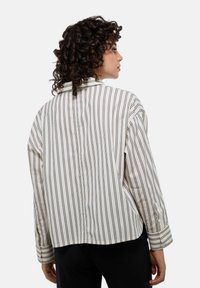 Chemise boutonnée rayée en crème clair avec de fines rayures noires. Elle présente un col, des manches longues, une coupe décontractée et un ourlet arrondi.