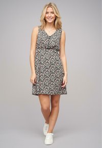 Robe fleurie avec un fond noir, ornée de petites fleurs roses. Elle a un décolleté en V, est sans manches et a une taille cintrée. Sneakers blanches.