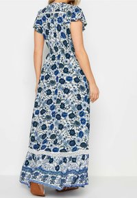 Maxiklänning med blommönster i blått och vitt, korta volangärmar, figursydd midja och en volangnederdel med spetsdetaljer.