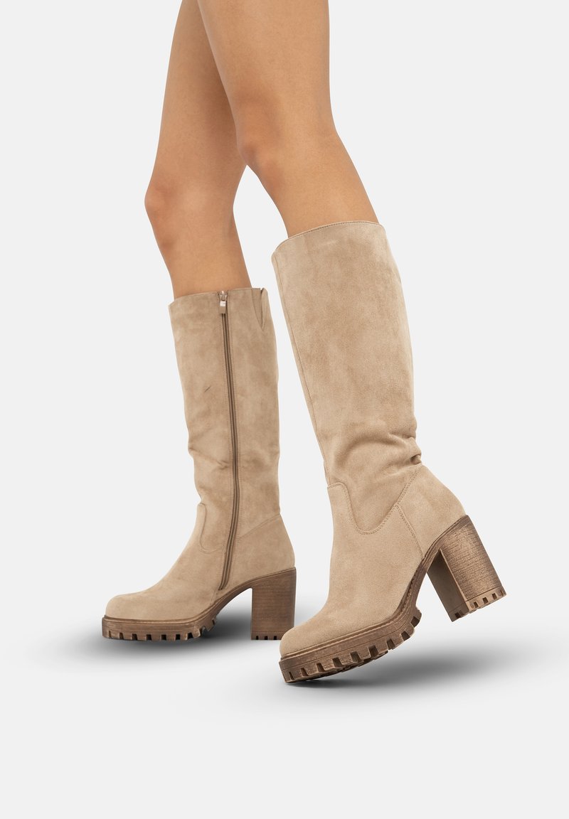 Botas altas de ante beige con tacón grueso, suela texturizada y detalle de cremallera lateral. Acabado suave con una silueta moderna.