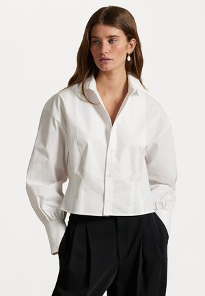 Weißes, tailliertes Button-up-Hemd aus Baumwollstoff mit großem Kragen, gerafften Ärmeln und glatter Textur. Kombiniert mit einer schwarzen Hose.
