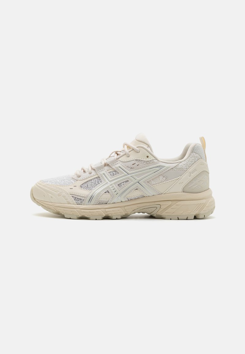Beige athletic shoe featuring a textured mesh upper, reinforced sides, and a sturdy rubber sole with a minimal design.