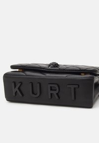 Czarna pikowana skórzana torba z zapięciem na klapę i wypukłymi literami "KURT" na dolnej stronie.