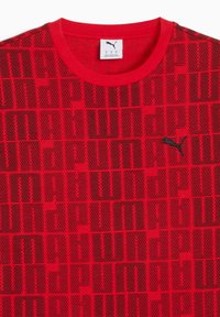 Red short-sleeve t-shirt with a textured pattern of black letters, featuring a black Puma logo on the left side of the chest.