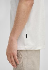 Witte T-shirt met korte mouwen en een gestructureerd oppervlak, met een gestikte zoom en een klein zwart label aan de zijkant, gecombineerd met lichtgestreepte broek.