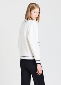 Maglione bianco con bordi e dettagli neri, caratterizzato da un colletto tondo, maniche lunghe e una vestibilità comoda, abbinato a pantaloni neri.