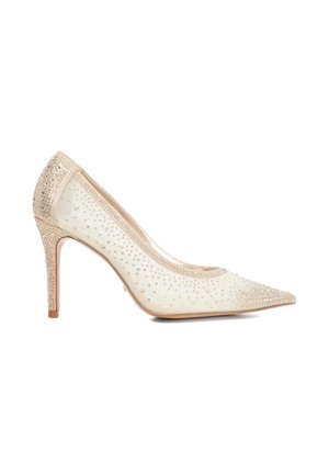 Zapato de tacón alto con punta afilada en tela color crema con superficie texturizada, adornado con strass transparentes. Presenta un tacón delgado y acentos en color beige.