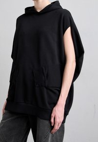 Svart, oversized hoodie med korta ärmar, som har två framfickor och ribbad nederkant, tillverkad av mjukt tyg.