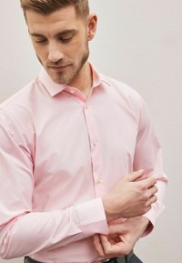 Helle rosa, langärmliges Hemd mit Knopfleiste und Kragen, das einen subtilen Glanz aufweist, mit Standardmanschetten und Knopfdetails auf der Vorderseite.