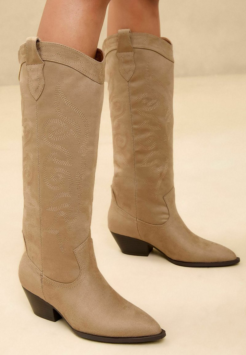 Beige suede cowboy saapad teravate varvastega, keskmise sääre kõrgusega, broderie spiraalmustriga ja madalate virnastatud kontsadega.