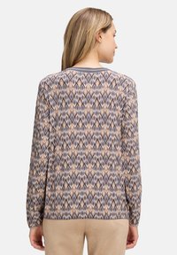 Long-sleeve top featuring a diamond pattern in neutral tones, with a ribbed collar and a relaxed fit. Made from a soft fabric.