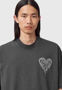 Sudadera de algodón gris oscuro con un gráfico de corazón grande y texto goteante en la parte izquierda del pecho. Cuello redondo y corte relajado.