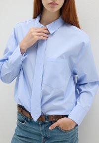 Hellblau gestreiftes Hemd mit spitzem Kragen und langen Ärmeln, kombiniert mit einer passenden Krawatte und getragen mit einem braunen Gürtel und Jeans.