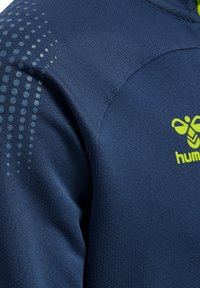 Mørkeblåt tekstureret stof med reflekterende prikket mønster på skulderen og en lys gul-grøn bi-logo og tekst på brystet.