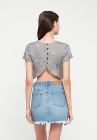Crop top rayé avec des accents floraux, fermeture par boutons dans le dos et dos ouvert. Associé à une mini-jupe en denim taille haute avec un ourlet effiloché.