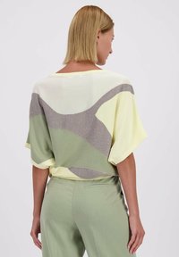 Korte mouwen gebreide top met een pastelgele, groene en zilveren patroon, met een relaxte pasvorm en ronde hals. Zachte textuur.