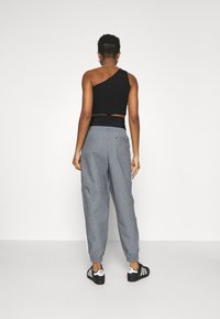 Top corto negro de un solo hombro con una cinturilla ajustada combinado con pantalones grises de cuadros sueltos con franjas blancas laterales. Zapatillas negras.