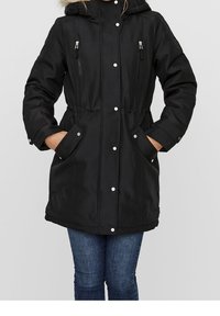 Parka noire avec une taille cintrée, une capuche détachable et une garniture en fausse fourrure. Comprend des boutons-pression, deux poches zippées et une texture lisse.