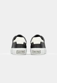 Svarte lær sneakers med hvite detaljer, med en glatt tekstur, avrundet form og merket etikett på hælen.