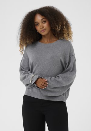 Maglione grigio oversize con maniche lunghe e morbide e scollatura rotonda. Tessuto a maglia e orlo a coste, abbinato a pantaloni scuri.