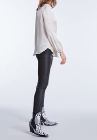 Pantaloni di pelle nera abbinati a una blusa di satin beige chiaro. Le calzature presentano un motivo a stampa serpente con accenti neri e un tacco spesso.