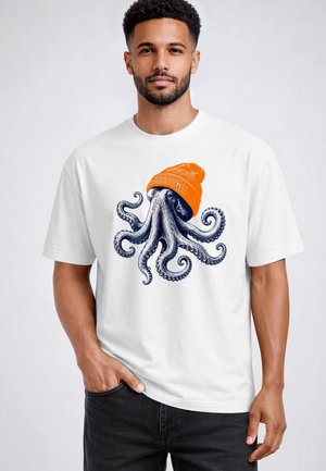 Man with beard and short curly hair wears white t-shirt featuring detailed octopus illustration wearing bright orange beanie hat.