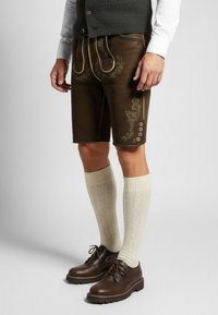 Bruine leren shorts met geborduurd bloemenpatroon, gouden accenten, zijzakken en knopen. Gecombineerd met crème knielange sokken en donkere schoenen.